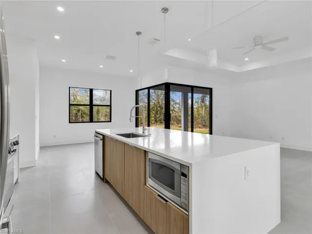 Kitchen with modern cabinets, light stone countertops, a large island with sink, stainless steel appliances, and a ceiling fan