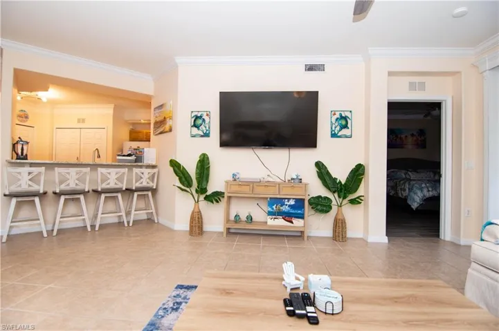 Living area features crown molding, a new ceiling fan, a large television, light colored and easy clean tile floors, a dining area and breakfast bar and comfortable furnishings and decor- all with a coastal flair.