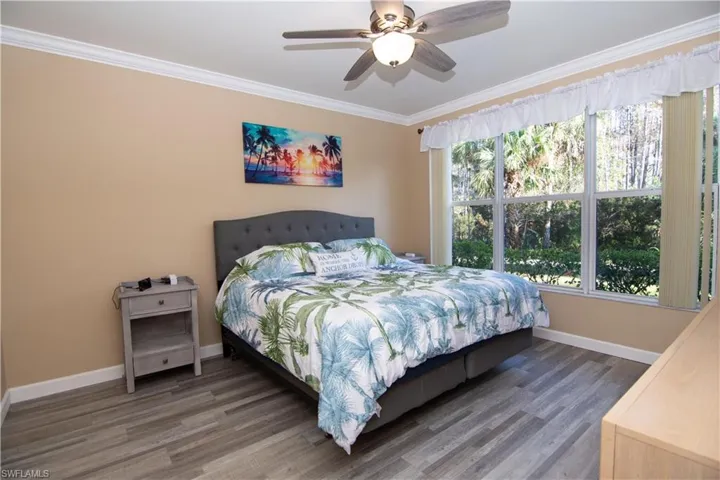 Spacious en suite Primary Bedroom features newly installed luxury vinyl plank flooring and ceiling fan, crown molding and a triple window overlooking the wooded Preserve.