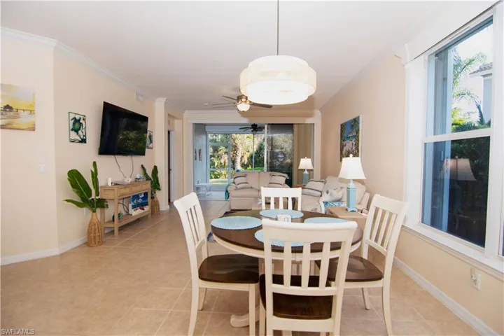 Living area features crown molding, a new ceiling fan, a large television, light colored and easy clean tile floors, a dining area and breakfast bar and comfortable furnishings and decor- all with a coastal flair.