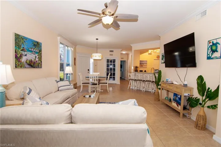 Living area features crown molding, a new ceiling fan, a large television, light colored and easy clean tile floors, a dining area and breakfast bar and comfortable furnishings and decor- all with a coastal flair.