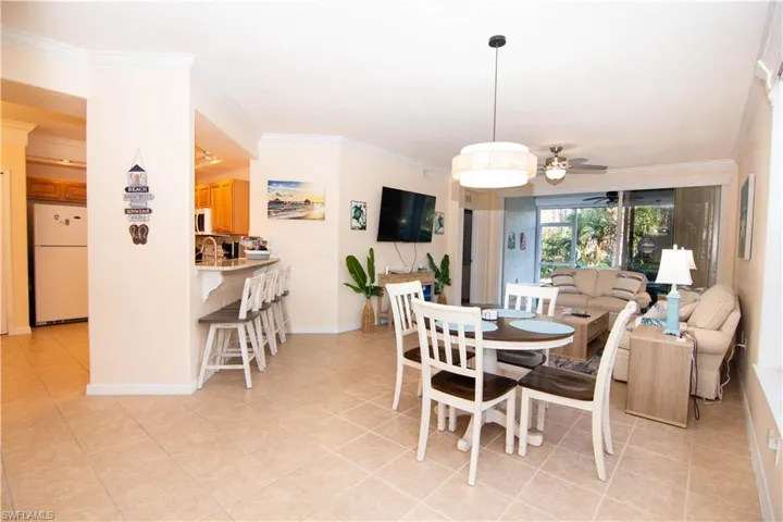 Living area features crown molding, a new ceiling fan, a large television, light colored and easy clean tile floors, a dining area and breakfast bar and comfortable furnishings and decor- all with a coastal flair.
