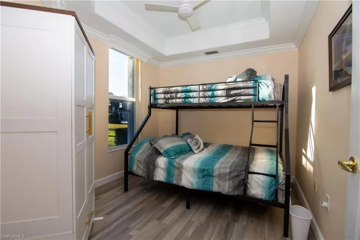 The Den is presently set up as an extra Bedroom that features luxury vinyl plank flooring, a raised ceiling, a new ceiling fan, crown molding, french doors and an armoire for storage.