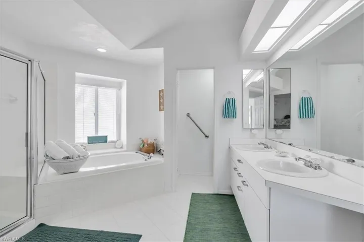 Full bath featuring double vanity, a shower stall, a garden tub, light tile patterned floors, and lofted ceiling
