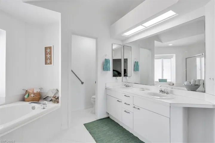 Bathroom featuring double vanity, a bath, a skylight, light tile patterned flooring, and a shower stall