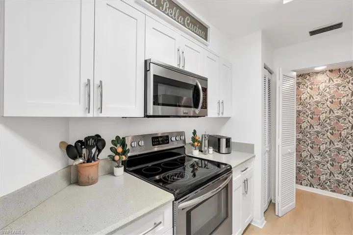 Kitchen with stainless steel appliances, white cabinetry, light stone counters, and light wood-style floors