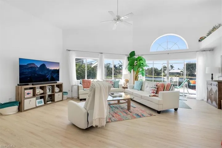 Living room with a high ceiling, a ceiling fan, and light wood-style floors