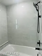 Bathtub with light-toned tiled surround, matte black rainfall showerhead, and matching fixtures