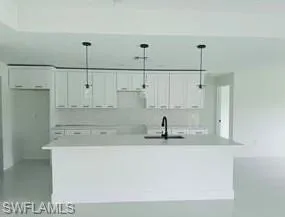 White shaker cabinetry, light-toned countertops, integrated sink, matte black faucet, and pendant lighting