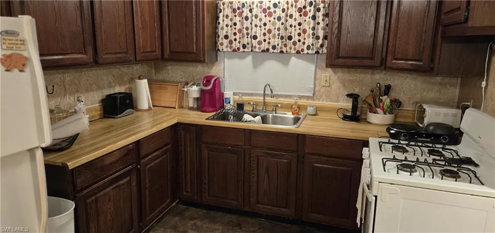 Kitchen featuring dark tile patterned floors, dark brown cabinetry, white appliances, and sink