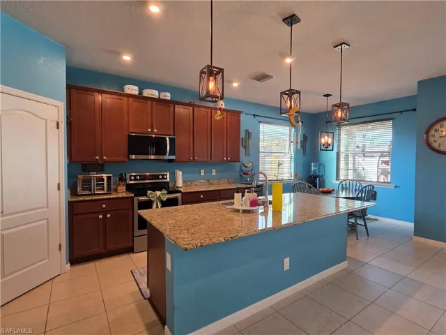Kitchen featuring stainless steel appliances, light tile patterned flooring, light stone countertops, hanging light fixtures, and a textured ceiling