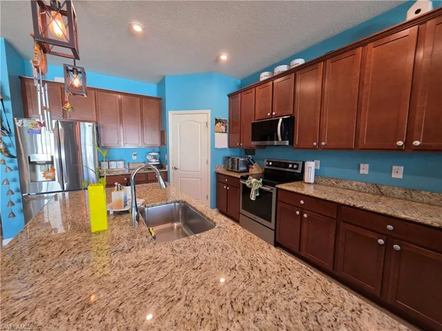 Kitchen featuring pendant lighting, stainless steel appliances, light stone counters, and a textured ceiling