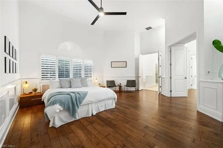 Bedroom with a decorative wall, a wainscoted wall, dark wood-style flooring, a high ceiling, and ceiling fan