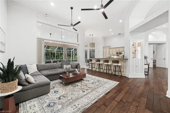 Living area featuring dark wood-style floors, arched walkways, ornamental molding, a high ceiling, and recessed lighting