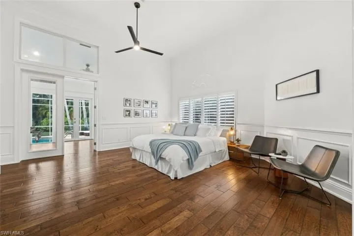 Bedroom with a decorative wall, dark wood finished floors, multiple windows, a wainscoted wall, and a high ceiling