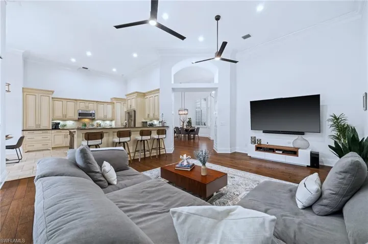 Living area with ornamental molding, dark wood-type flooring, a high ceiling, a ceiling fan, and recessed lighting