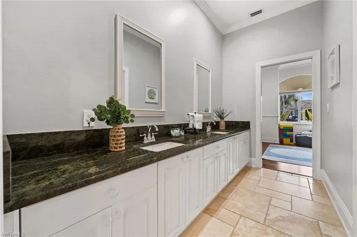 Bathroom with double vanity, stone tile flooring, and crown molding