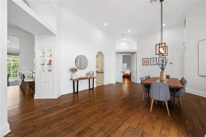 Dining room with dark wood-style flooring, ornamental molding, arched walkways, recessed lighting, and a high ceiling
