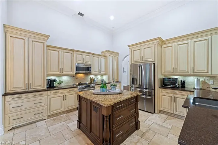 Dual tone kitchen with arched walkways, stainless steel appliances, dark stone countertops, ornamental molding, and two tone cabinetry