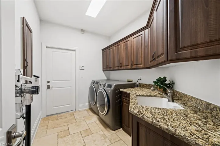 Laundry room with cabinet space, washing machine and clothes dryer, and stone tile floors