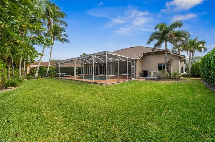 Rear view of property featuring a lanai, an outdoor pool, a lawn, and stucco siding
