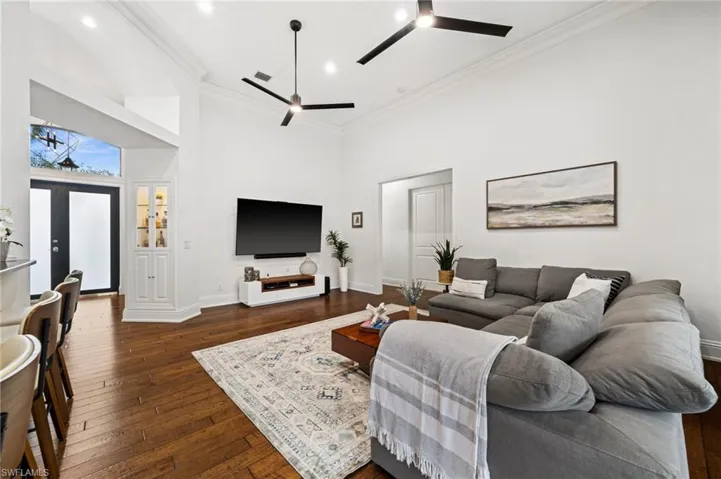 Living area with dark wood-type flooring, a high ceiling, ornamental molding, and ceiling fan