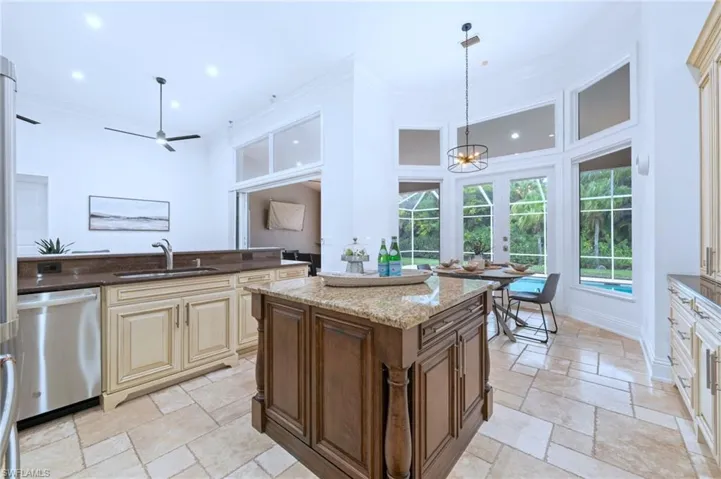 Dual tone kitchen with dark stone counters, dishwasher, two tone cabinets, stone tile floors, and ornamental molding