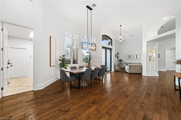 Dining area with dark wood-type flooring, a high ceiling, suspended lighting, and ornamental molding