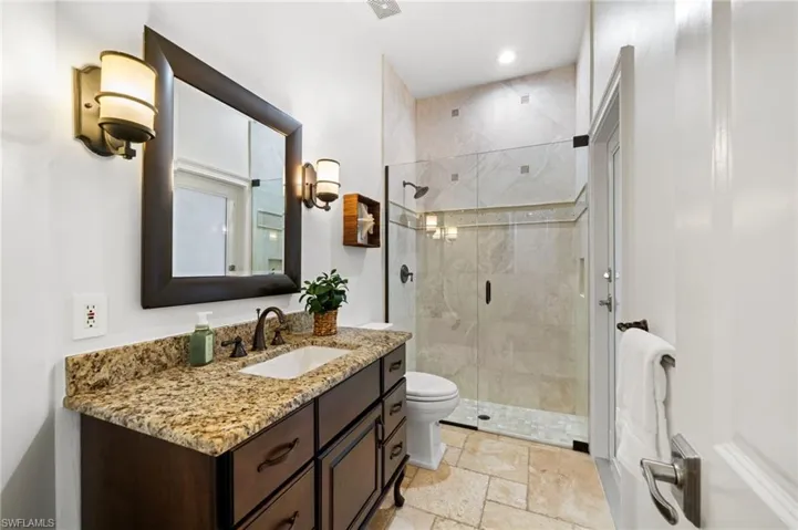 Full bathroom with access from the pool area with vanity, a shower stall, stone tile flooring, and recessed lighting