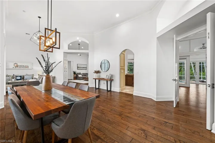 Dining space featuring dark wood-type flooring, ornamental molding, arched walkways, a high ceiling, and hanging lights