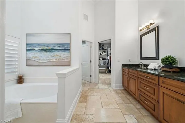 Full bath with vanity, a high ceiling, stone tile flooring, a bath, and a spacious closet