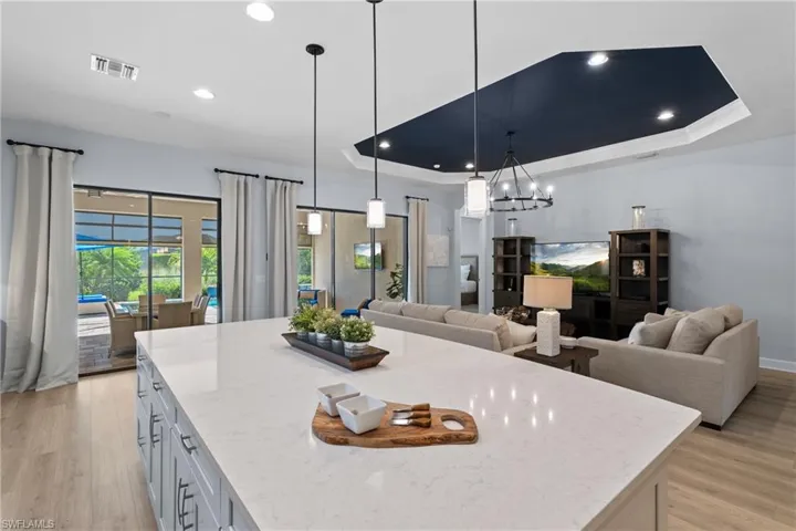 Kitchen with light stone counters, a raised ceiling, open floor plan, light wood-type flooring, and visible vents