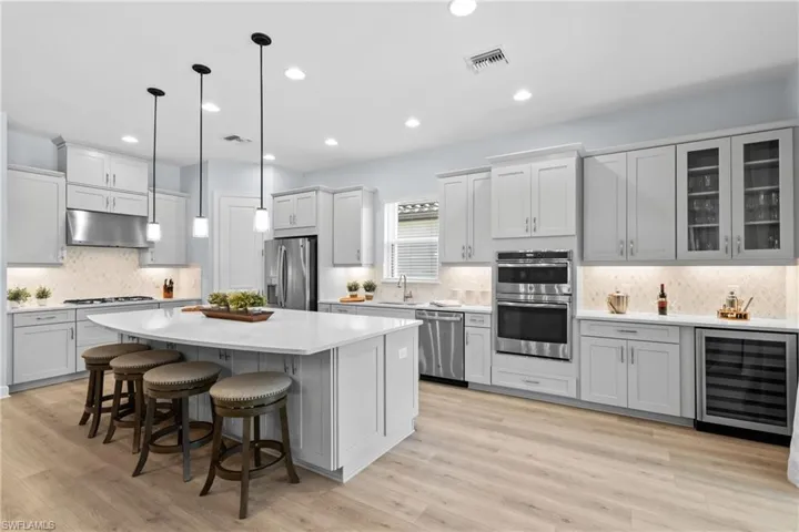 Kitchen with light countertops, visible vents, wine cooler, appliances with stainless steel finishes, and under cabinet range hood