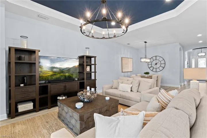 Living area with a raised ceiling, wood finished floors, visible vents, arched walkways, and an inviting chandelier