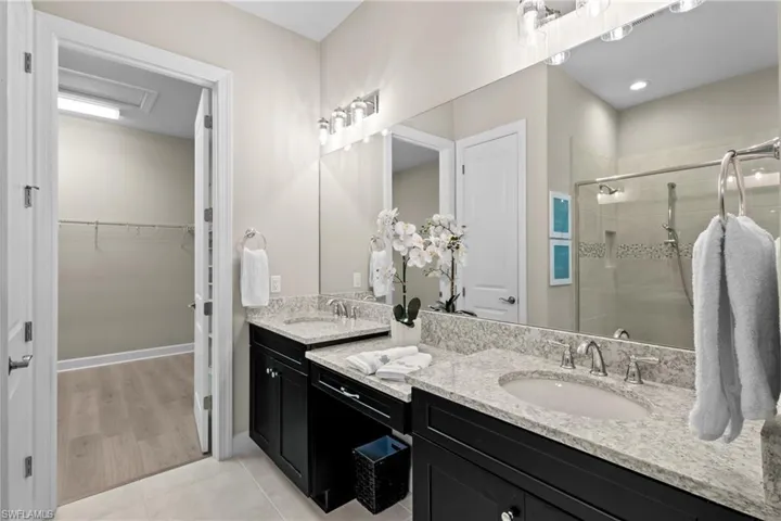 Bathroom featuring a stall shower, double vanity, a spacious closet, and a sink