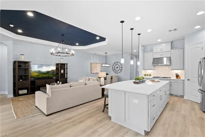 Kitchen with light countertops, freestanding refrigerator, a raised ceiling, light wood-style flooring, and under cabinet range hood