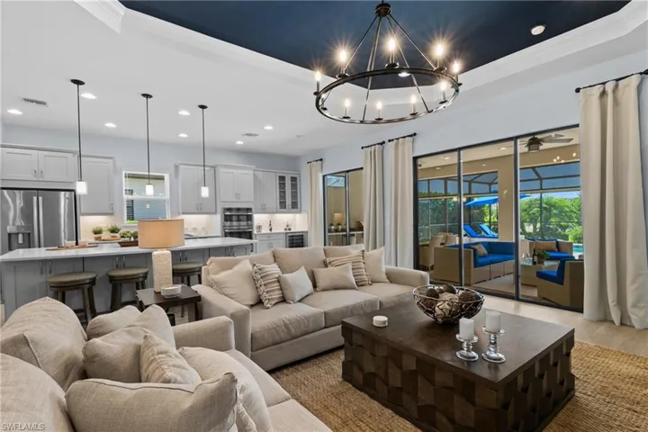 Living room featuring a tray ceiling, a chandelier, recessed lighting, light wood-style floors, and ornamental molding