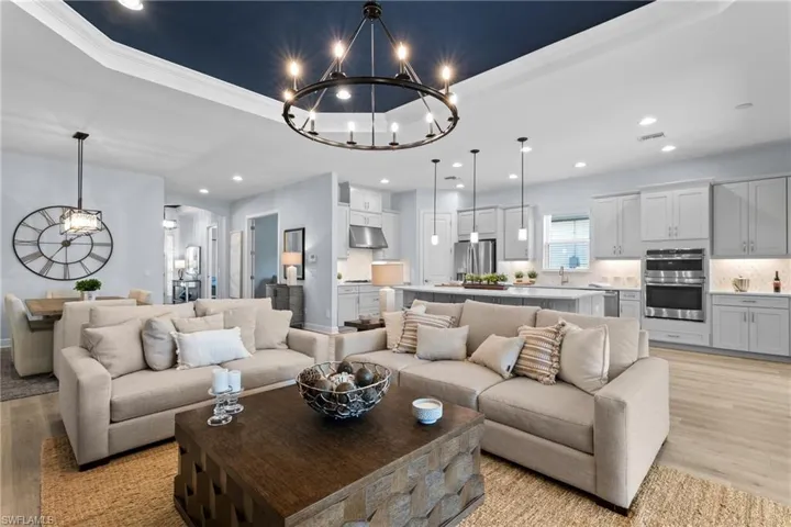 Living area featuring a tray ceiling, recessed lighting, light wood finished floors, visible vents, and a notable chandelier