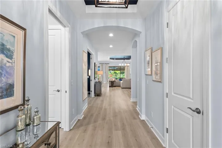 Hall with light wood-style flooring, baseboards, arched walkways, and recessed lighting