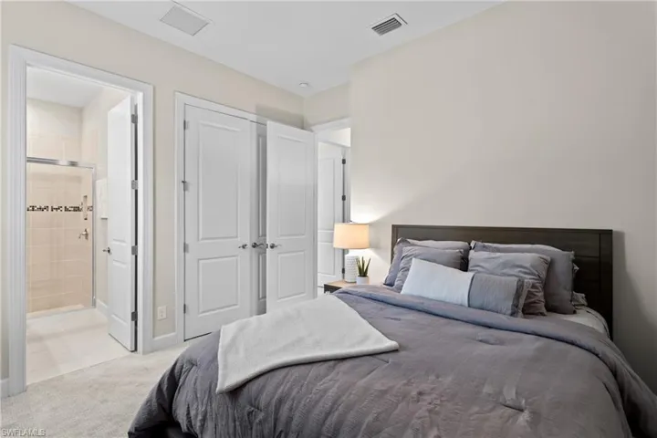 Bedroom with connected bathroom, light colored carpet, visible vents, and baseboards