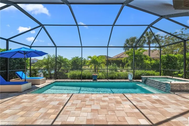 View of pool with glass enclosure, a pool with connected hot tub, and a patio