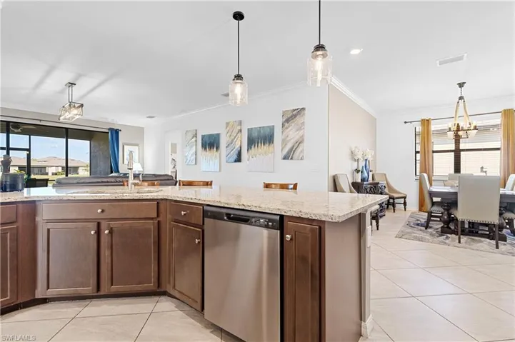 Kitchen with dark brown cabinets, light tile patterned flooring, pendant lighting, stainless steel dishwasher, and crown molding
