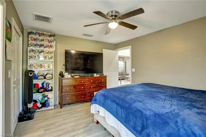 Spacious room featuring wood-finish flooring, a ceiling fan with integrated lighting, and a white interior door