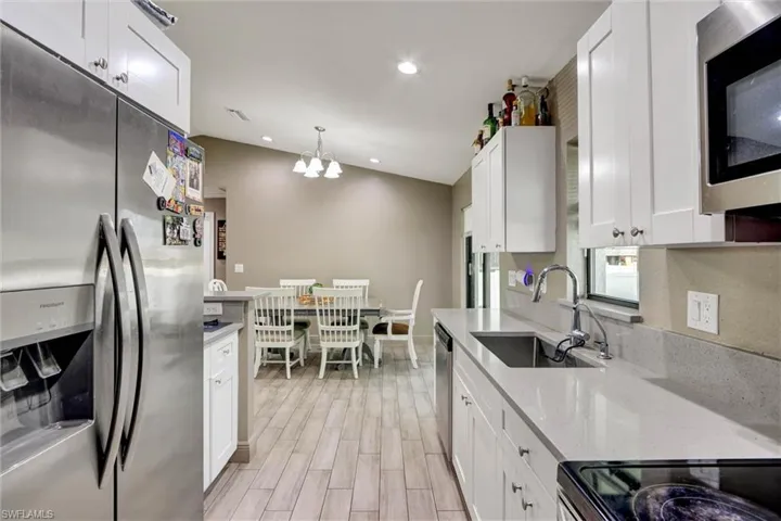 Modern kitchen featuring white shaker cabinetry, light-toned countertops, a stainless steel refrigerator, and wood-finish flooring