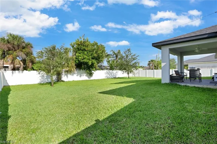 Expansive backyard featuring a lush lawn, white privacy fencing, and mature tropical landscaping