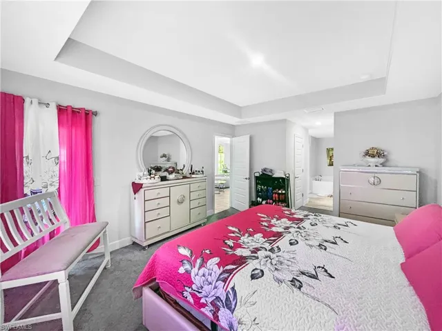 Bedroom featuring a tray ceiling, dark colored carpet, and connected bathroom