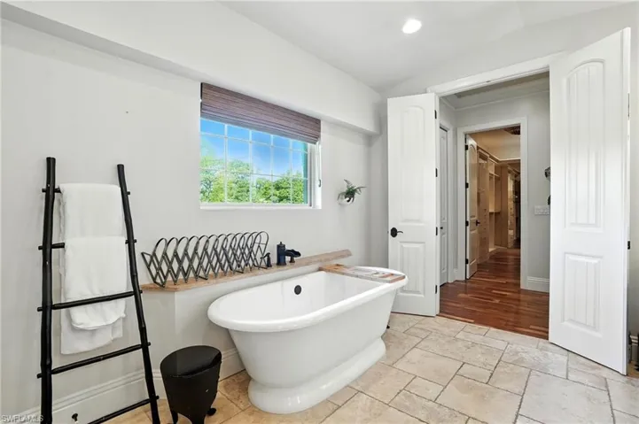 Bathroom featuring a soaking tub, stone tile floors, recessed lighting, and vaulted ceiling - Virtually Edited Image