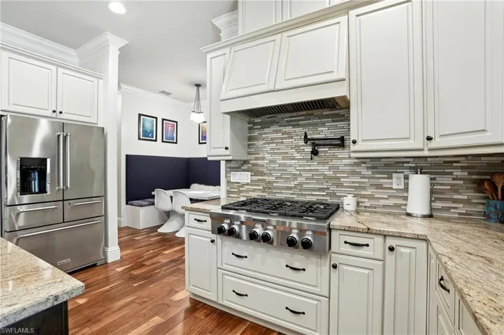 Kitchen featuring appliances with stainless steel finishes, light stone counters, ornamental molding, dark wood-style floors, and white cabinetry - Virtually Edited Image
