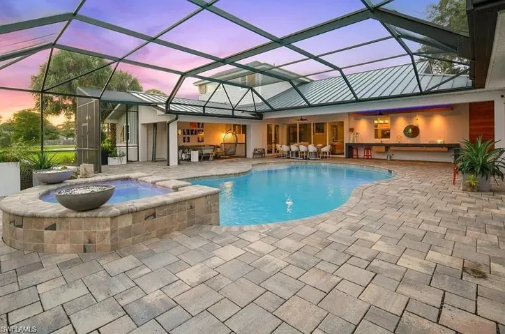 View of pool with glass enclosure, a pool with connected hot tub, a sunroom, and a patio area - Virtually Edited Image