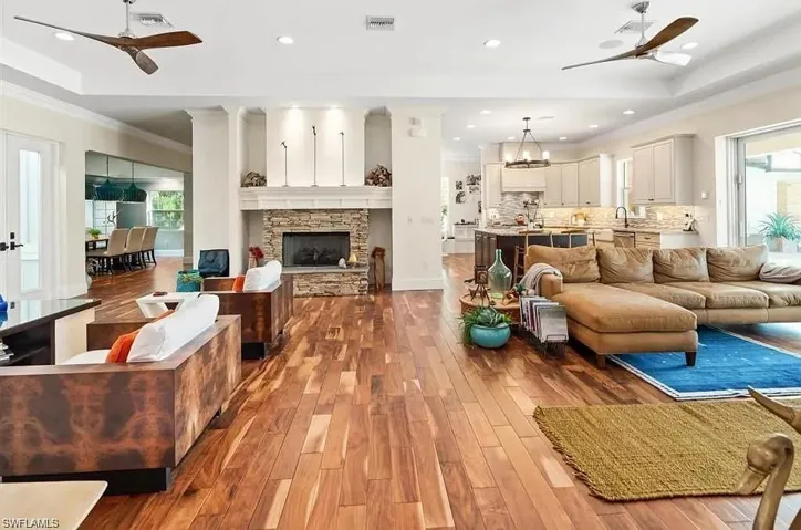Living area with a ceiling fan, recessed lighting, a raised ceiling, dark wood-style floors, and ornamental molding - Virtually Edited Image
